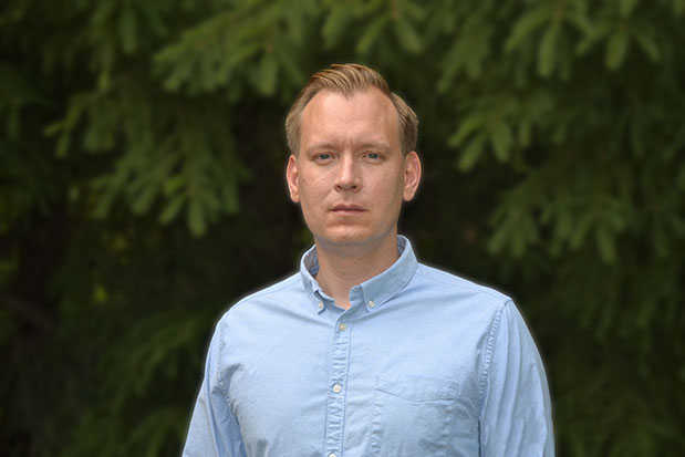 David Magård i ljusblå skjorta står framför en grönskande granskog.