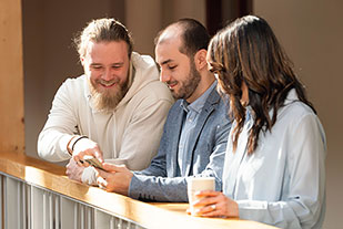 Tre glada personer sitter i en soffa och pratar.